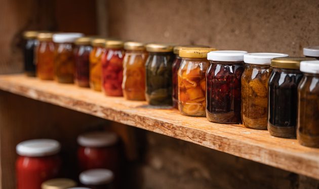 Row of pickled vegetables, jams and chutneys on a wooden shelf.